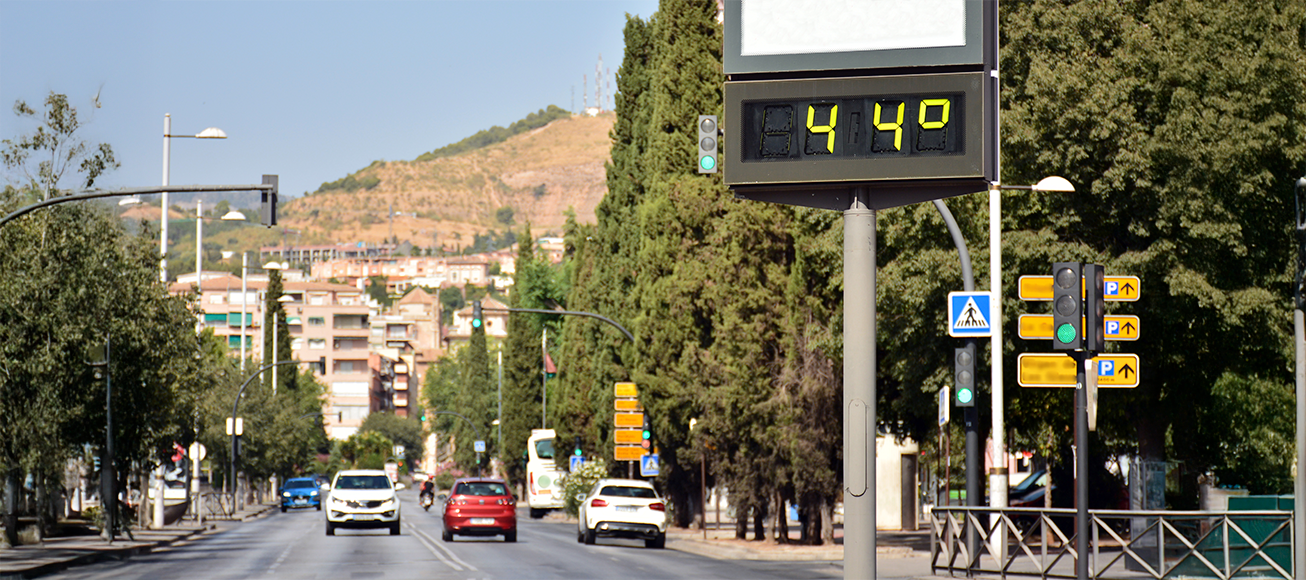 Termómetro urbano marca 44 grados en avenida soleada con tráfico ligero, señalando ola de calor.