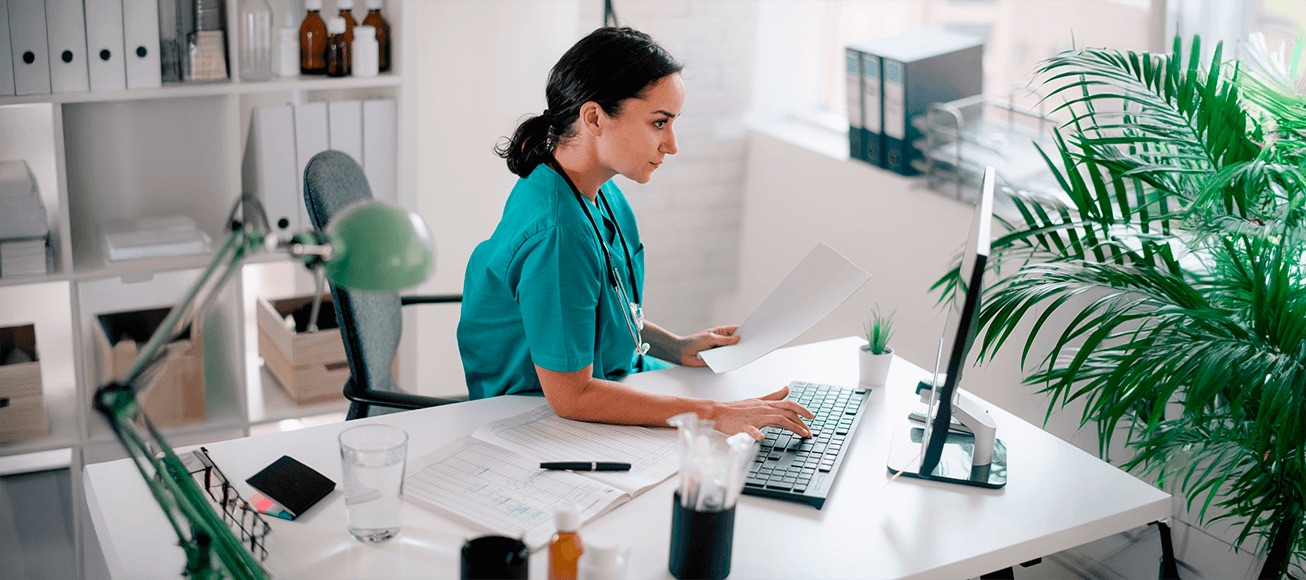 Profesional sanitario trabaja en ordenador revisando documentos en entorno clinico, destacando ciberseguridad y proteccion de datos.