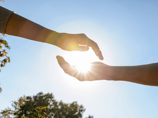Dos manos al aire libre enmarcan el sol, simbolizando equilibrio en la exposición solar.