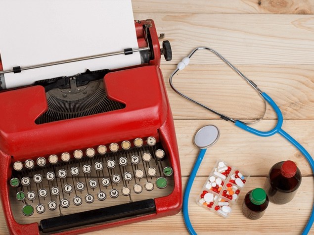 Máquina de escribir roja con papel, estetoscopio azul, pastillas y frascos sobre mesa de madera.