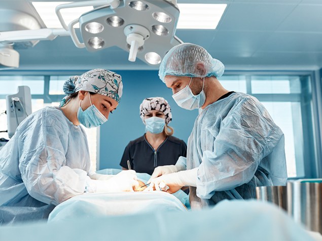 Doctora observa a otros dos médicos durante una operación.