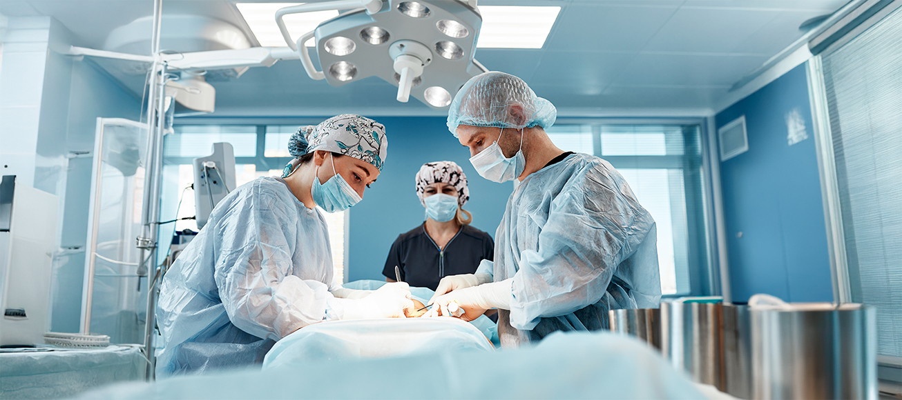 Doctora observa a otros dos médicos durante una operación.