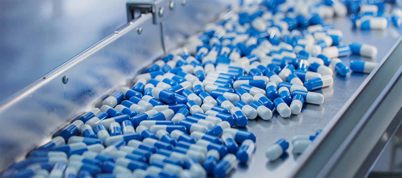 Cinta de produccion con capsulas azules y blancas en una fabrica farmaceutica moderna.