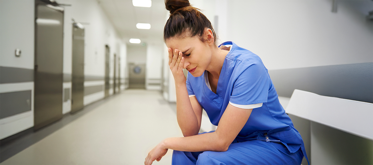 Sanitaria desolada en el pasillo de un hospital.