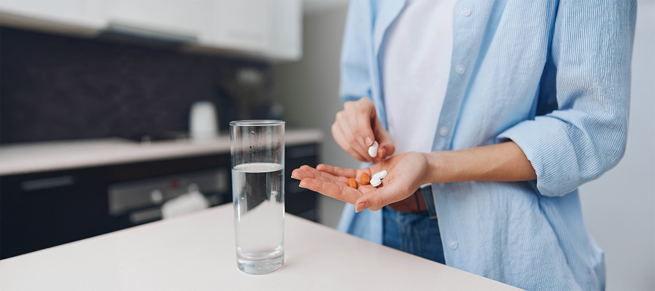 Paciente con unas pastillas en su mano y un vaso de agua.