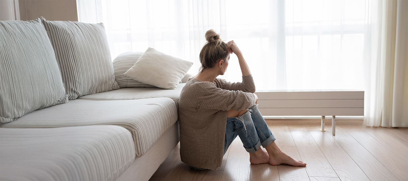 Mujer sola en un salón mirando hacia una ventana.
