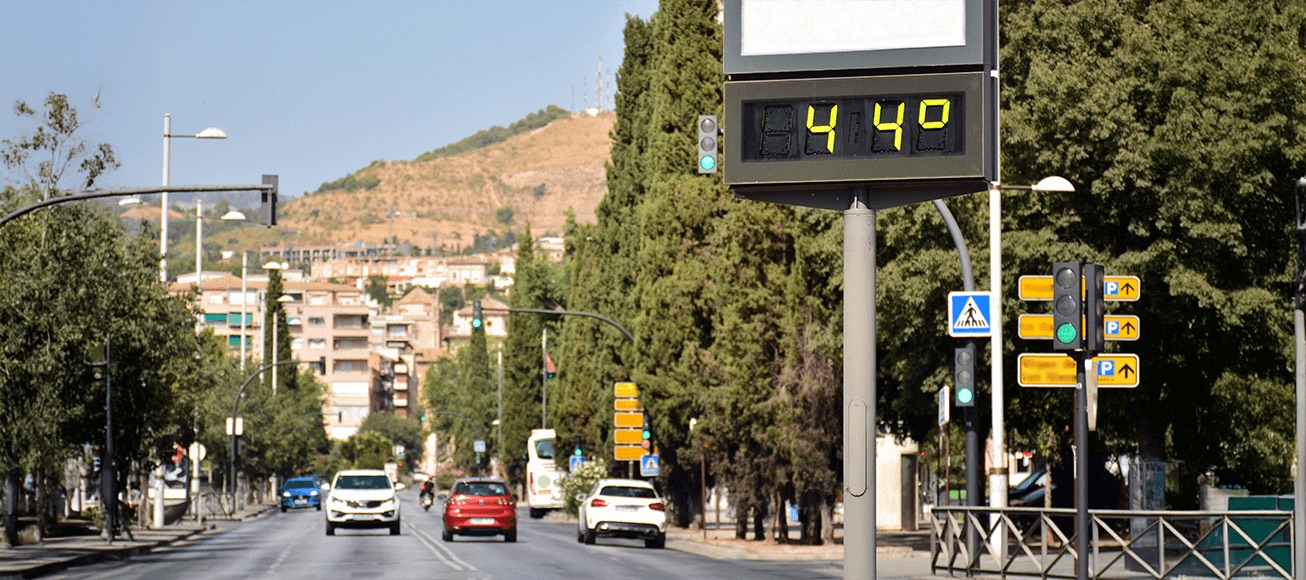 Termómetro urbano marca 44 grados en avenida soleada con tráfico ligero, señalando ola de calor.