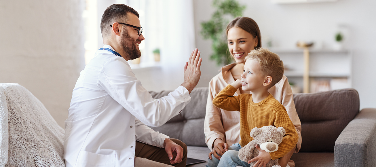 Médico de familia atendiendo a un niño en brazos de su madre.