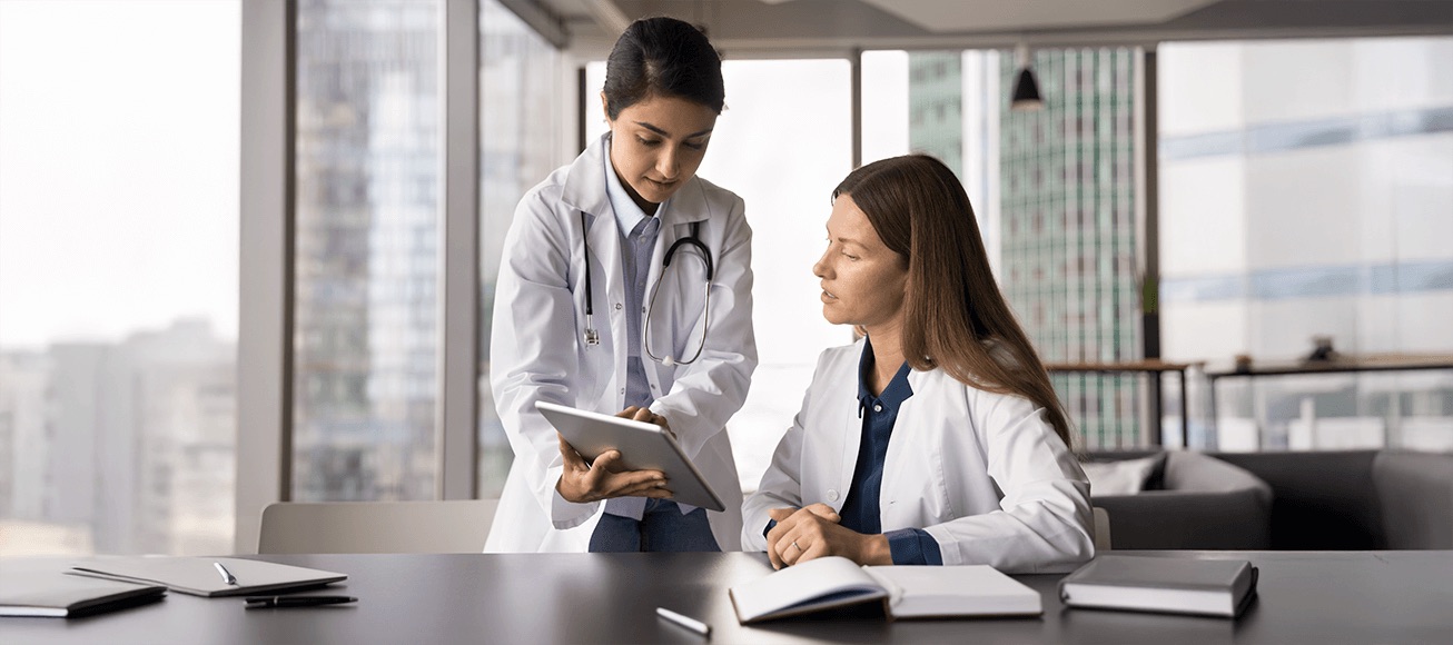 Tutora medica orienta a residente durante tutoria, revisando caso clinico en tablet.