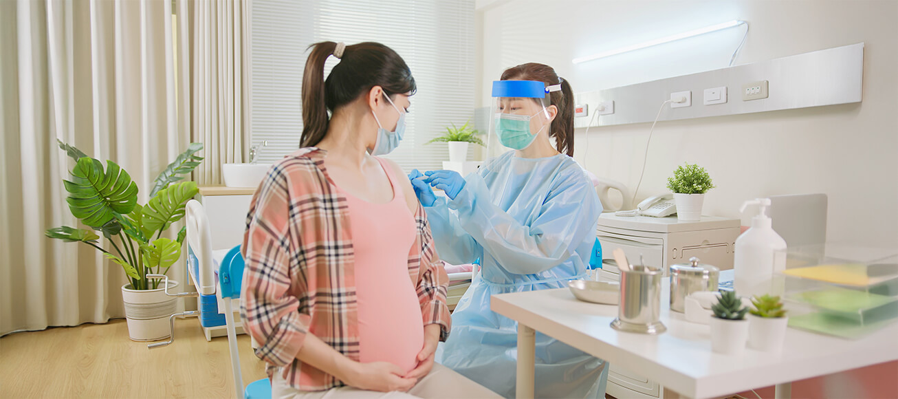 Profesional sanitario con equipo protector aplica inyección a mujer embarazada durante ensayo clínico en consulta