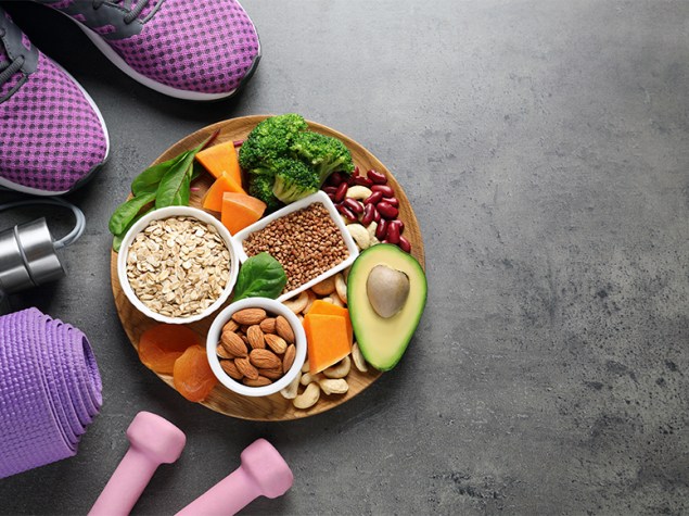 Alimentos servidos en un bowl junto con unas mancuernas y unas zapatillas deportivas.