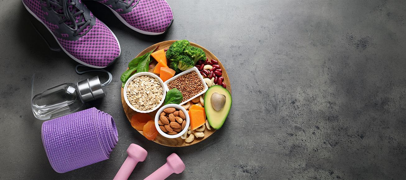 Alimentos servidos en un bowl junto con unas mancuernas y unas zapatillas deportivas.