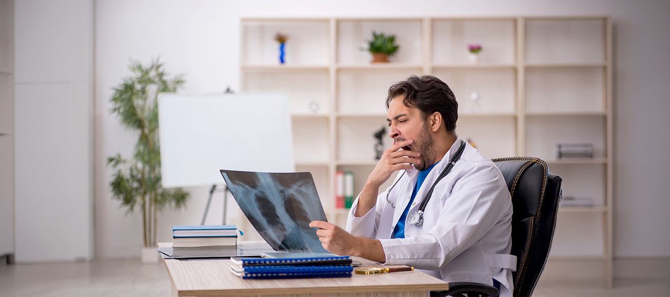 Médico analizando una radiografía mientras bozteza en una guardia.